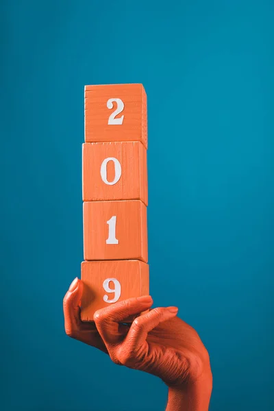 Partial view of woman holding coral wooden cubes with 2019 numbers on blue background, color of 2019 concept — Stock Photo