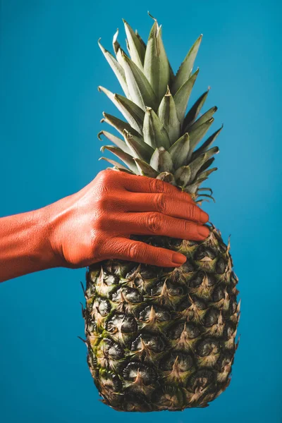 Cropped view of woman holding pineapple in coral colored hand on blue background, color of 2019 concept — Stock Photo