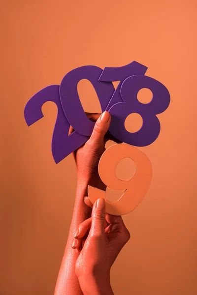 Partial view of coral colored female hands with violet paper cut 2018 numbers and coral number 9 on coral background, color of 2019 concept — Stock Photo