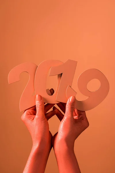 Vue partielle des mains féminines de couleur corail avec du papier découpé numéros 2019 sur fond corail, couleur du concept 2019 — Photo de stock