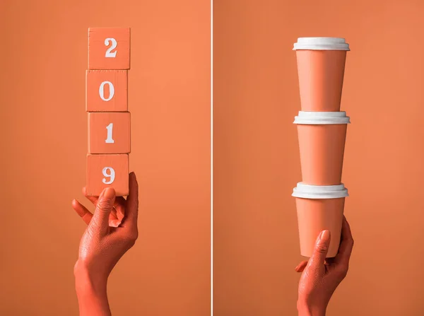 Cubes en bois de corail avec numéros 2019 et pile de tasses en papier de corail dans les mains des femmes sur fond de corail divisé, couleur du concept 2019 — Photo de stock