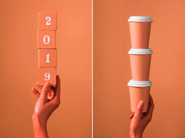 Cubos de madera de coral con números 2019 y pila de tazas de papel de coral en manos femeninas sobre fondo de coral dividido, concepto de color de 2019 — Stock Photo