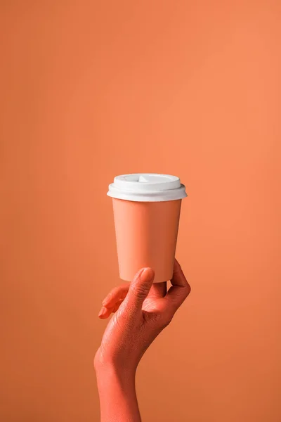 Partial view of female hand with coral paper cup on coral background, color of 2019 concept — Stock Photo