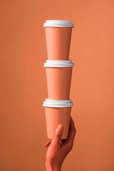 Vista recortada de la mano femenina con pila de tazas de papel de coral sobre fondo de coral, concepto de color de 2019 — Stock Photo