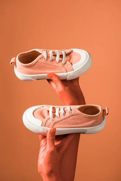 Vista recortada de la mujer sosteniendo zapatillas de deporte sobre fondo de coral, color de 2019 concepto - foto de stock