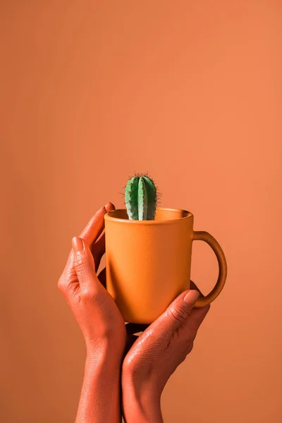 Teilansicht einer Frau mit korallenfarbener Kaffeetasse mit grünem Kaktus auf korallenfarbenem Hintergrund, Konzept 2019 — Stockfoto
