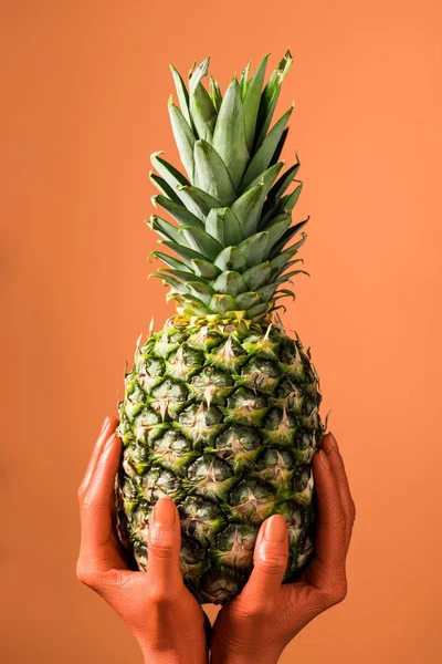 Partial view of coral colored female hands with pineapple fruit on coral background, color of 2019 concept — Stock Photo