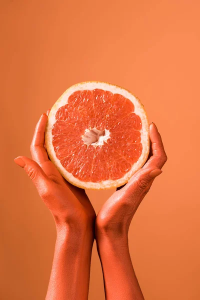 Vista recortada de las manos femeninas de color coral con la mitad de pomelo sobre el fondo de coral, concepto de color de 2019 - foto de stock