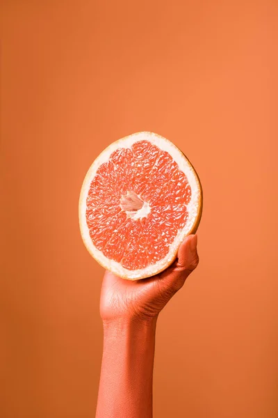 Обрезанный вид кораллового цвета женской руки с грейпфрутом наполовину на коралловом фоне, цвет концепции 2019 года — стоковое фото