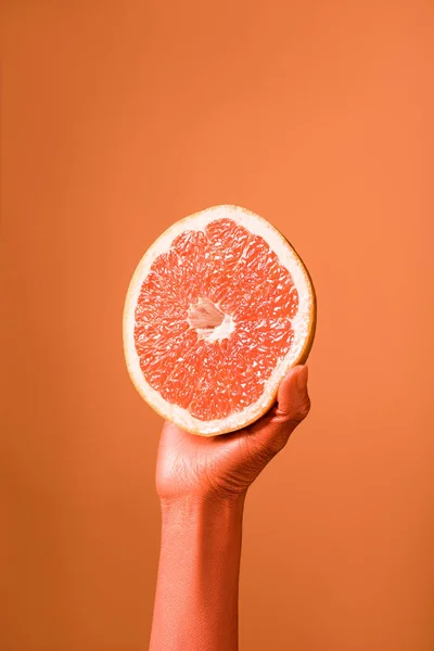 Vue recadrée de la main féminine de couleur corail avec moitié pamplemousse sur fond corail, couleur du concept 2019 — Photo de stock