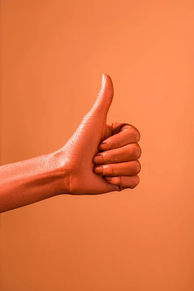 Vista recortada de la mujer que muestra el pulgar hacia arriba sobre el fondo de coral, el color del concepto 2019 - foto de stock