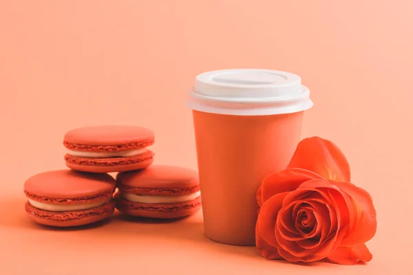 Délicieux macarons et tasse en papier sur fond corail, couleur du concept 2019 — Photo de stock