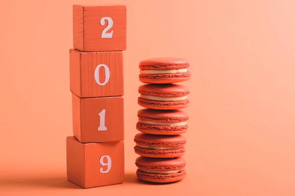 Stack of wooden cubes with 2019 numbers and macarons on coral background, color of 2019 concept — Stock Photo