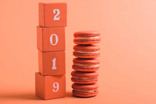 Stapel von Holzwürfeln mit Zahlen und Macarons 2019 auf Korallenhintergrund, Farbe des Konzepts 2019 — Stockfoto