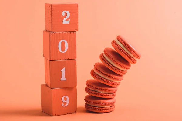 Stapel von Holzwürfeln mit Zahlen und Macarons 2019 auf Korallenhintergrund, Farbe des Konzepts 2019 — Stockfoto