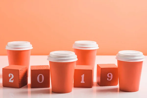 Copos de descarte de coral e cubos de madeira com números 2019 e copos de papel na superfície branca, cor do conceito 2019 — Fotografia de Stock