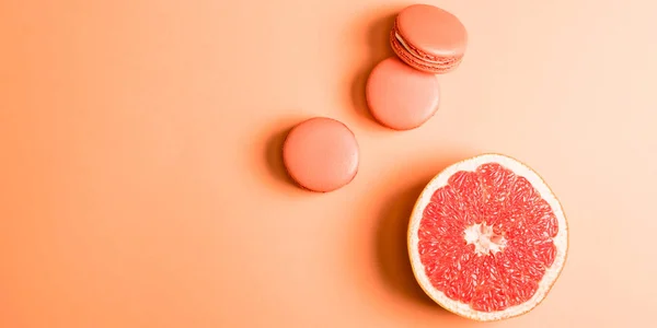 Vue du dessus des macarons de corail et de la moitié de pamplemousse sur fond de corail, couleur du concept 2019 — Photo de stock