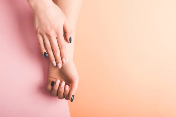 Vista recortada de las manos femeninas con uñas de color rosa y negro sobre fondo bicolor, concepto de color de 2019 - foto de stock
