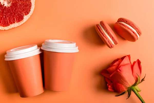 Tazas de papel de coral, flor de rosa, macarrones y la mitad de pomelo sobre el fondo de coral, el color del concepto 2019 - foto de stock