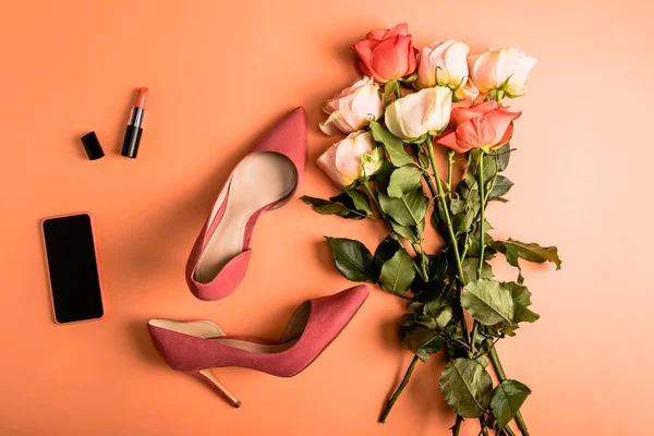 Bouquet de roses corail, chaussures, rouge à lèvres corail et smartphone sur fond corail, concept couleur de l'année 2019 — Photo de stock