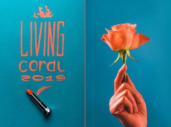 Color del año 2019 letras manuscritas con lápiz labial de coral, y vista parcial de la mano femenina de color coral con rosa de coral sobre fondo dividido azul — Stock Photo