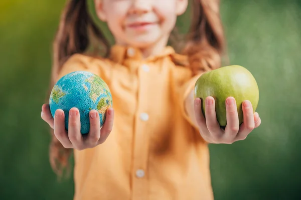 Enfoque selectivo de niño sosteniendo globo modelo y manzana sobre fondo borroso, concepto del día de la tierra - foto de stock