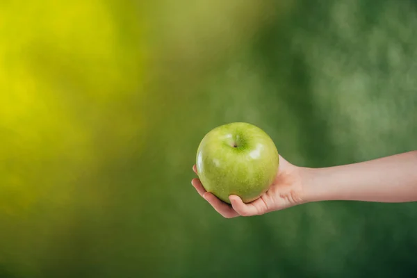 Vista parcial de la mano del niño con manzana sobre fondo borroso, concepto del día de la tierra - foto de stock