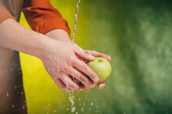 Teilansicht eines Mannes, der unter pustendem Wasser Apfel wäscht, auf verschwommenem Hintergrund, Earth Day Konzept — Stockfoto