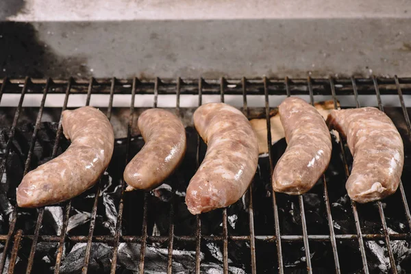 Embutidos frescos crudos cocinando en la parrilla de barbacoa con brasas quemadas - foto de stock