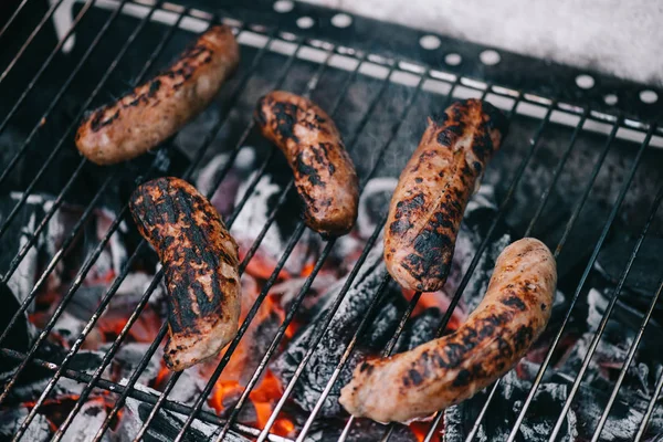 Enfoque selectivo de salchichas a la parrilla dispersas deliciosas en humo en la rejilla de barbacoa - foto de stock