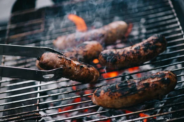 Foco seletivo de pinças com linguiça grelhada no churrasco — Fotografia de Stock