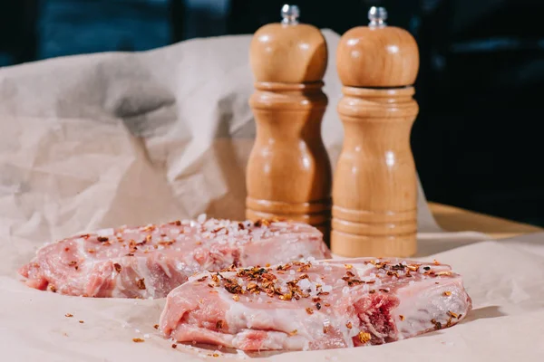 Selective focus of raw fresh steaks with seasoning and salt and pepper mills on paper — Stock Photo