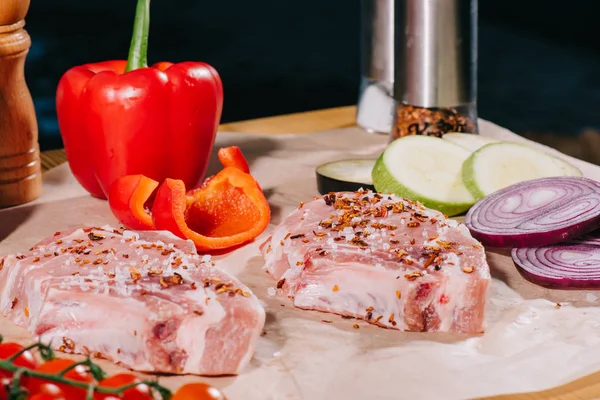 Close up of raw juicy steaks with seasoning and fresh ripe vegetables on paper — Stock Photo