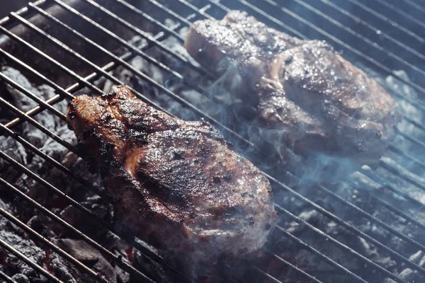Selective focus of juicy tasty steaks grilling on hot coals with smoke — Stock Photo