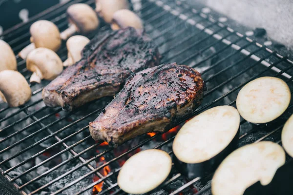 Selektiver Fokus auf saftige, schmackhafte Steaks vom Grill auf heißen Kohlen mit Pilzen und geschnittenen Auberginen — Stockfoto