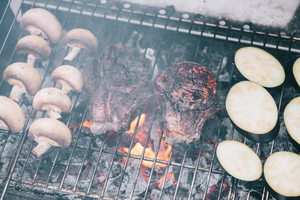 Selective focus of juicy tasty steaks grilling on bbq grid with mushrooms and sliced eggplant — Stock Photo