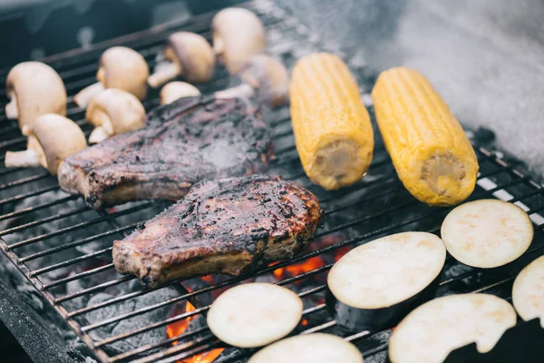 Selektiver Fokus auf saftige, schmackhafte Steaks vom Grill auf Grillrost mit Pilzen, Mais und geschnittenen Auberginen — Stockfoto