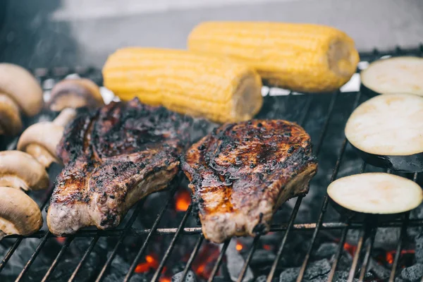 Selective focus of tasty steaks grilling on bbq grid with mushrooms, corn and sliced eggplant — Stock Photo