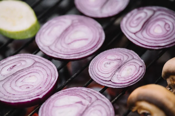 Selective focus of raw onion slices, zucchini and mushrooms grilling on barbecue grid — Stock Photo