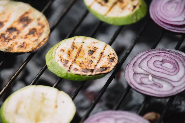 Selective focus of onion and zucchini slices grilling on barbecue grid — Stock Photo
