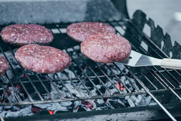 Selective focus of spatula and uncooked fresh burger cutlets grilling on bbq grid — Stock Photo