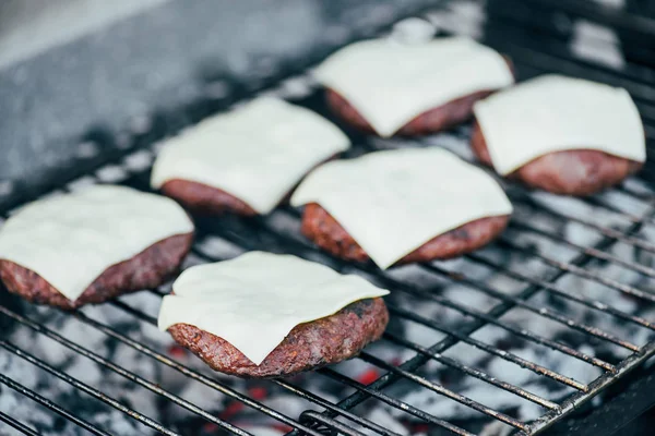 Enfoque selectivo de chuletas de hamburguesas frescas con queso a la parrilla en la rejilla de barbacoa - foto de stock