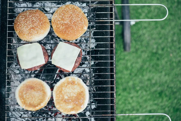 Vue du dessus de délicieux hamburgers frais ingrédients grillades sur grille de barbecue — Photo de stock