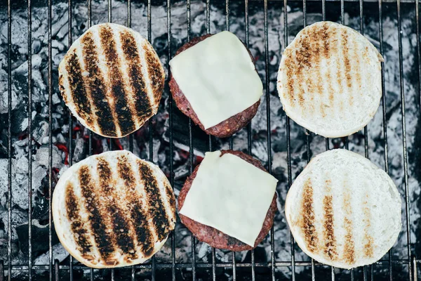 Вид на вкусные свежие ингредиенты гамбургеров гриля на сетке барбекю — стоковое фото