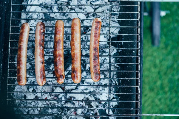 Vista dall'alto di gustose salsicce alla griglia su barbecue grado griglia su sfondo erba verde — Foto stock