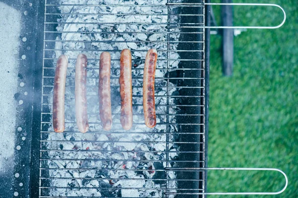Vista dall'alto di gustose salsicce alla griglia su barbecue grado griglia su sfondo erba verde — Foto stock