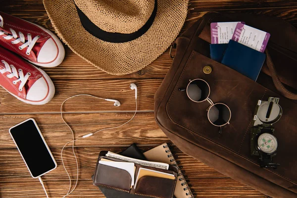 Top view of smartphone with earphones, passports with tickets and accessories with keds on wooden surface — Stock Photo