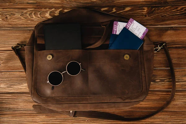 Vue du dessus du sac marron en cuir avec lunettes de soleil et passeports avec billets — Photo de stock