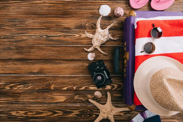 Top view of summer accessories on suitcase with retro film camera and seashells around on wooden background — Stock Photo