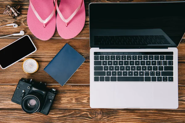 Vista superior de chinelos rosa, câmera de filme vintage, bússola, passaporte, smartphone com fones de ouvido e laptop na superfície de madeira — Fotografia de Stock